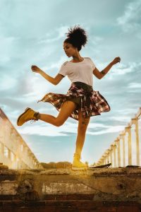 a young black women in shorts and a white t-shirt with a plaid shirt tied around her waist, dances on the steps 