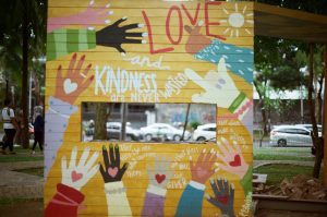 art work on a yellow background with lots of hands painted in different colours sending blessings to those who give and those who receive. The artwork is in a park.