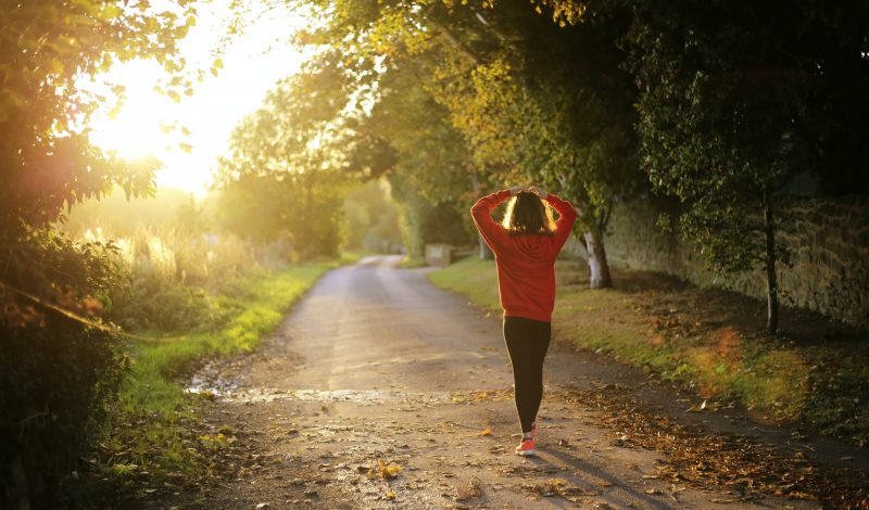 Woman in orange jumper walking in the morning sun down a track lined with trees