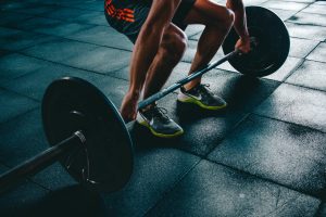 Cropped image of a man in shorts and trainers performing the deadlift exercise with the barbell on black mats 